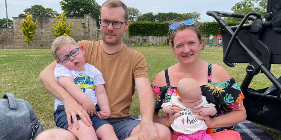 A family including a boy with complex needs and his baby sister, are smiling at the camera
